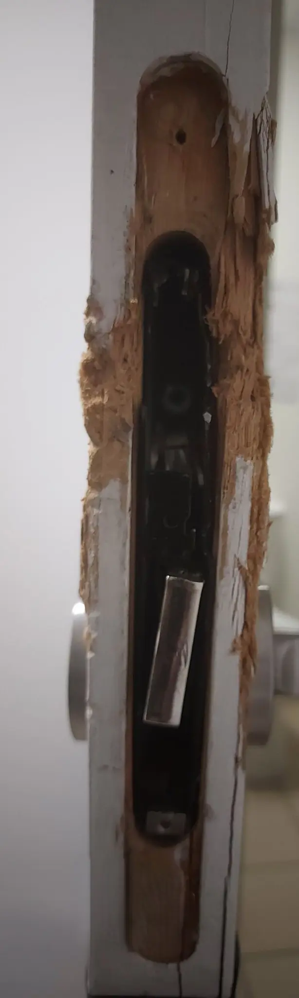 Chant d’une porte blanche éclaté autour du boîtier de serrure, bois arraché, pêne tordu
