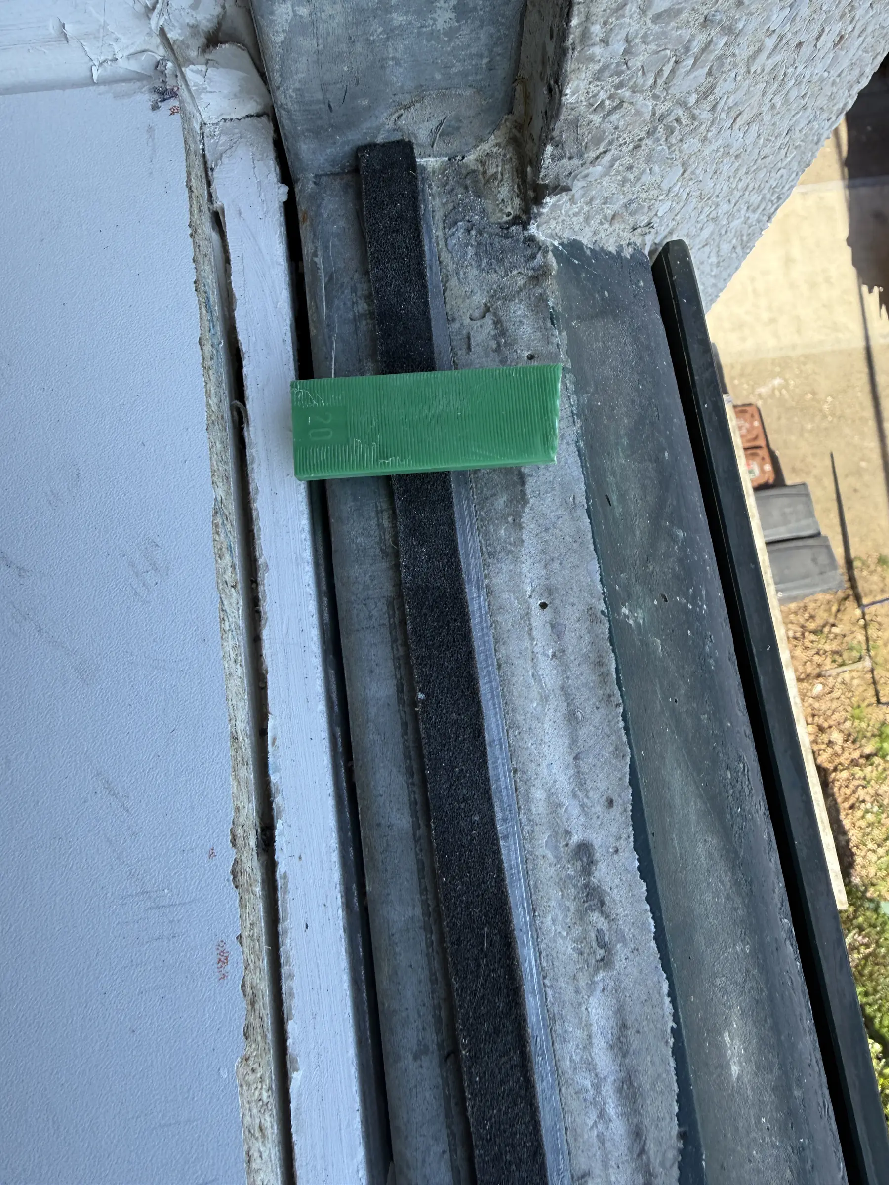 Vue plongeante sur un appui en béton : bande d’étanchéité noire et cale verte posées avant la fenêtre