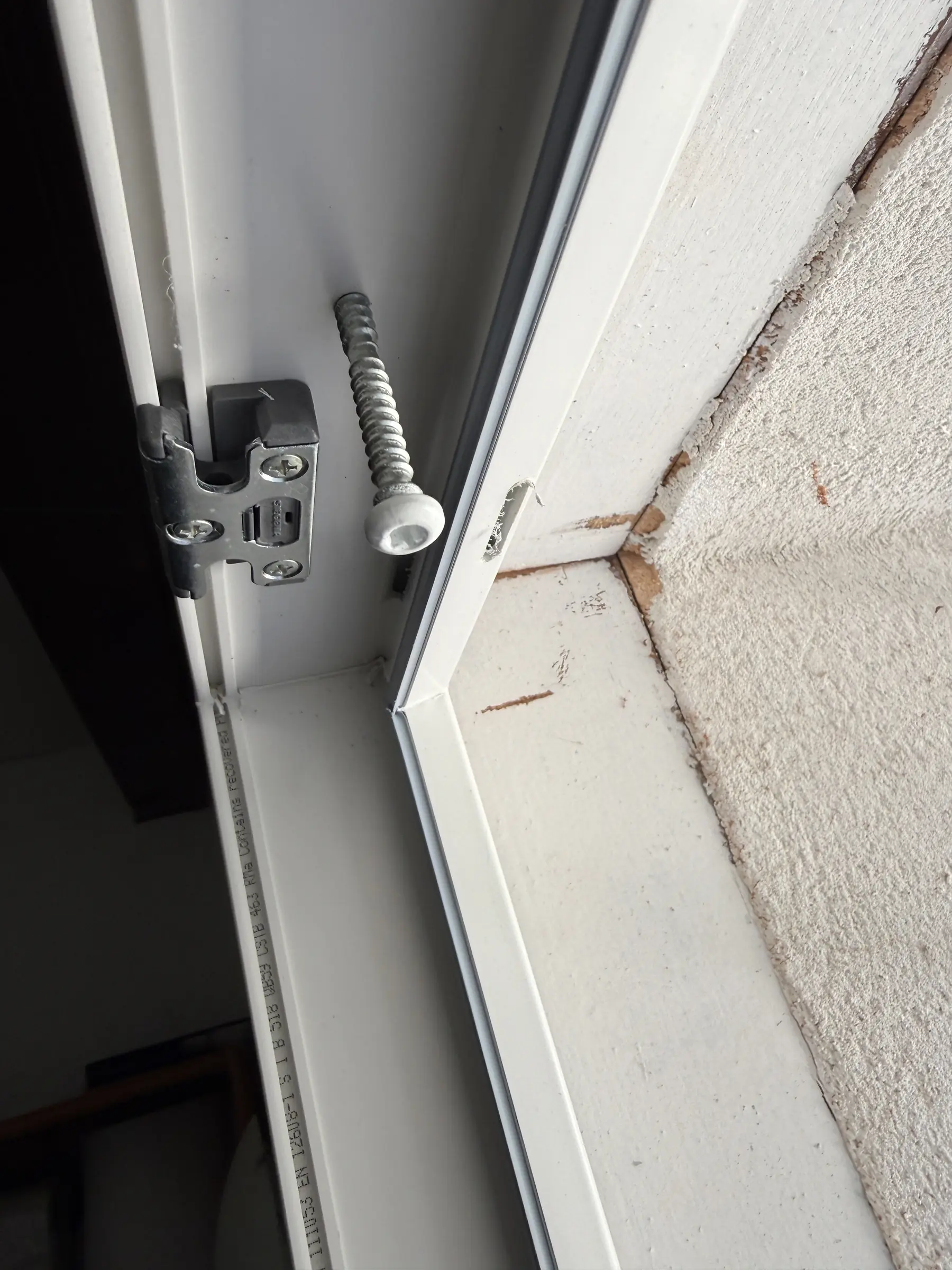 Gros plan d’un dormant PVC blanc neuf contre l’ancien cadre en bois peint, paumelle et vis de fixation