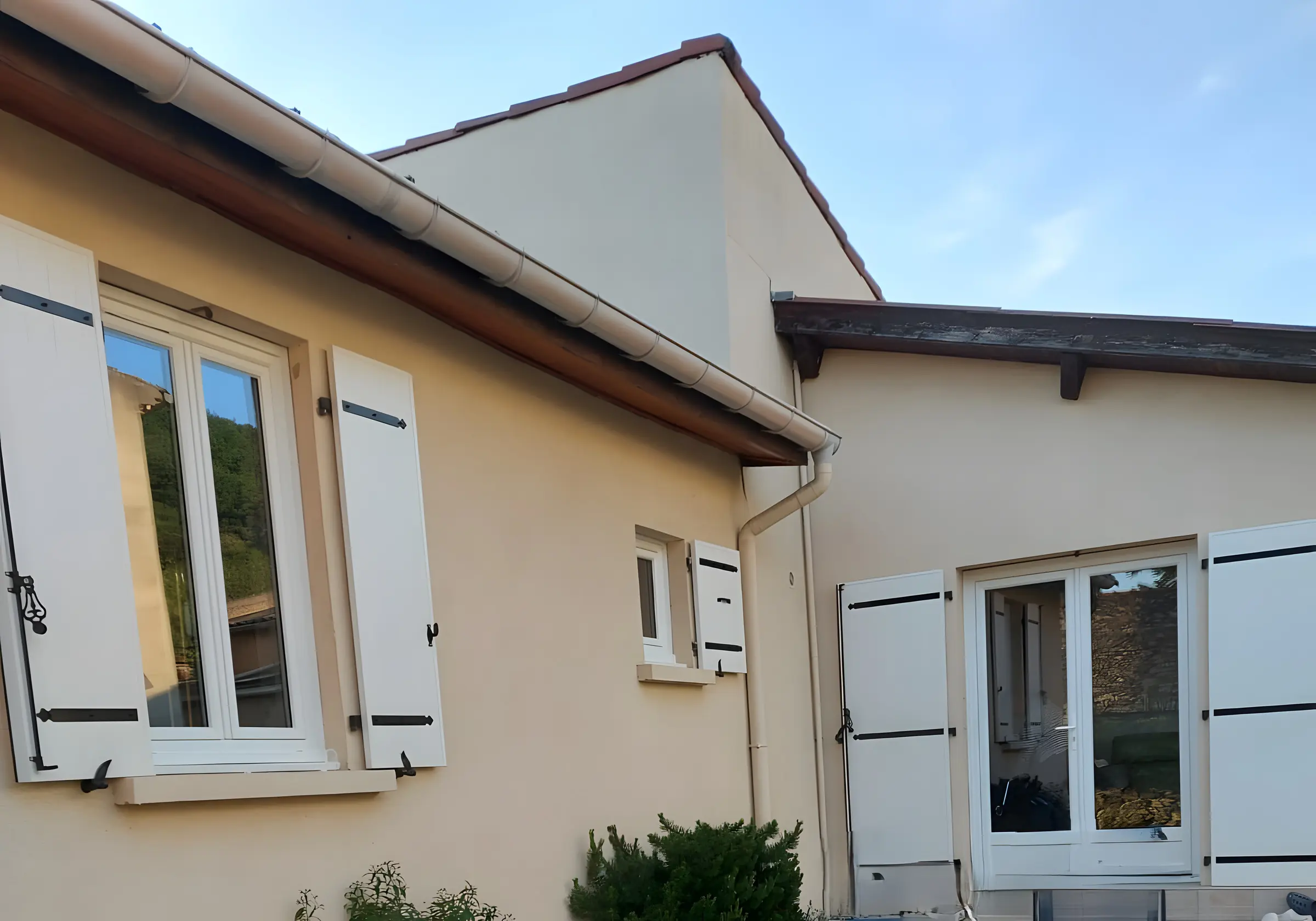Façade de maison : fenêtres et porte-fenêtre PVC blanches entre des volets battants blancs à pentures noires