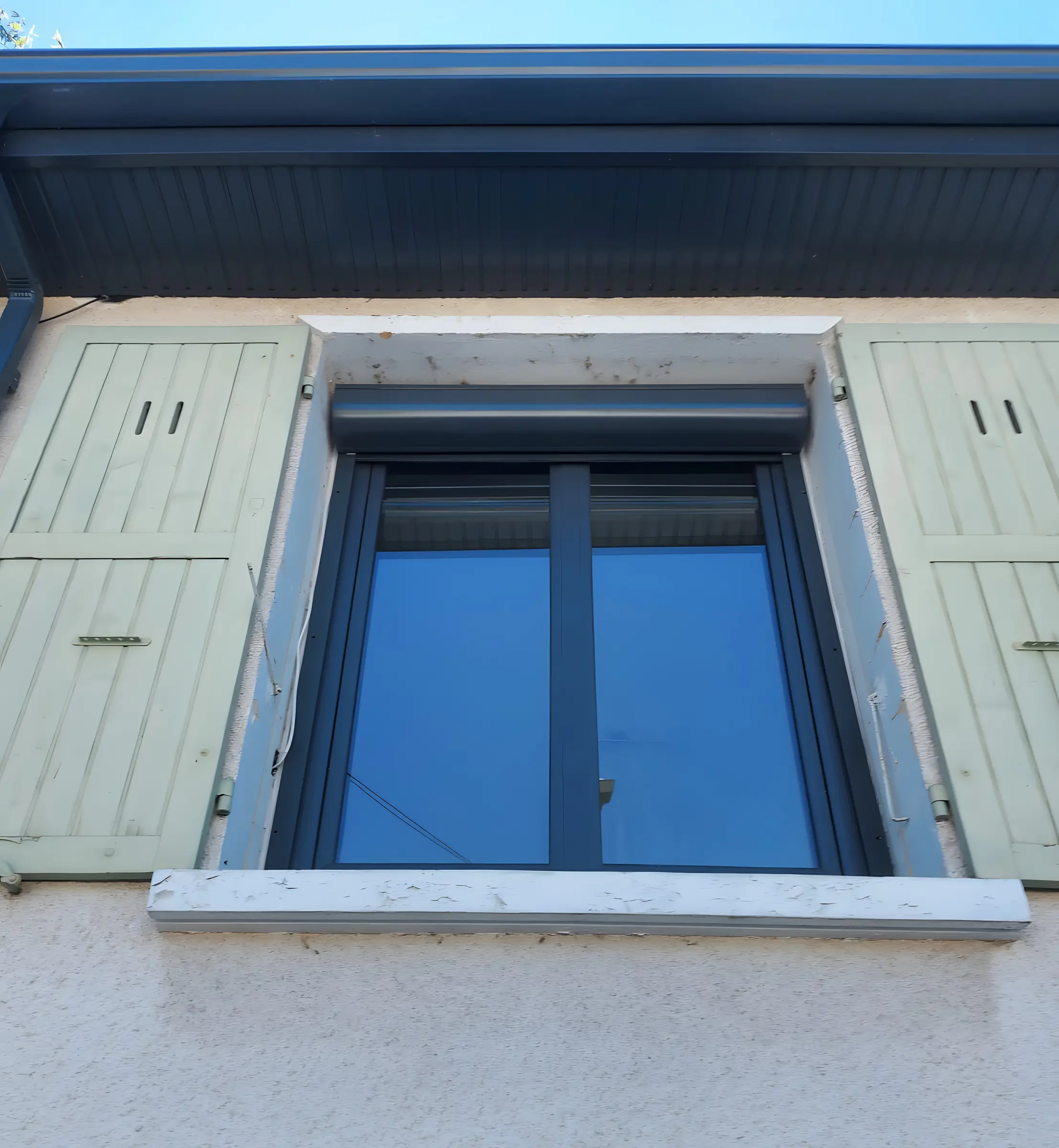 Fenêtre gris anthracite à deux vantaux et coffre de volet roulant anthracite, entre deux volets battants vert pâle