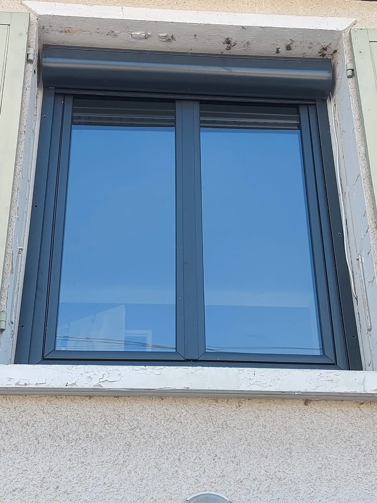 Fenêtre gris anthracite à deux vantaux sous un coffre de volet roulant anthracite, volets battants vert pâle ouverts