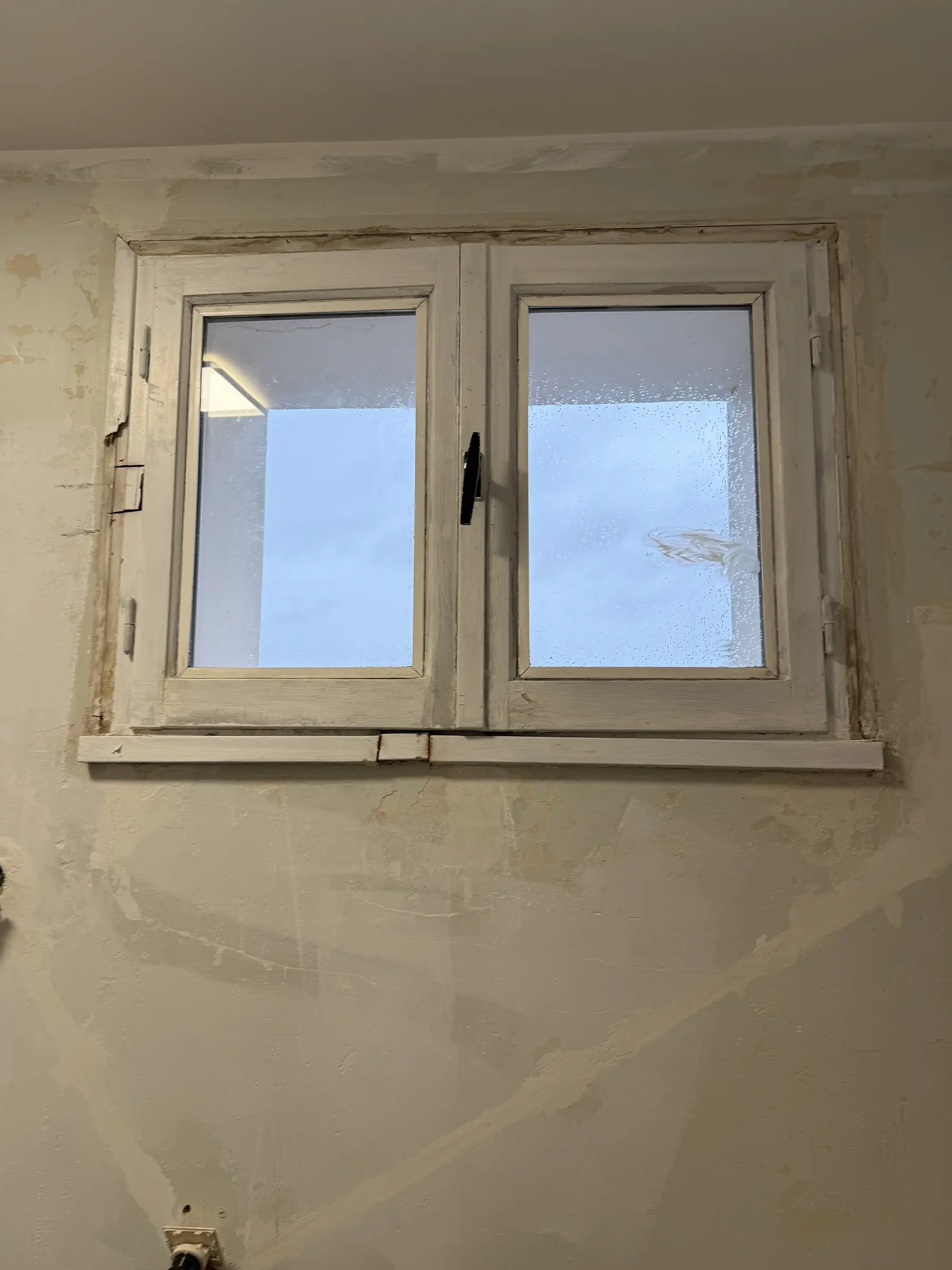 Vieille fenêtre en bois blanc à deux vantaux vue de l’intérieur, peinture usée, appui en bois abîmé