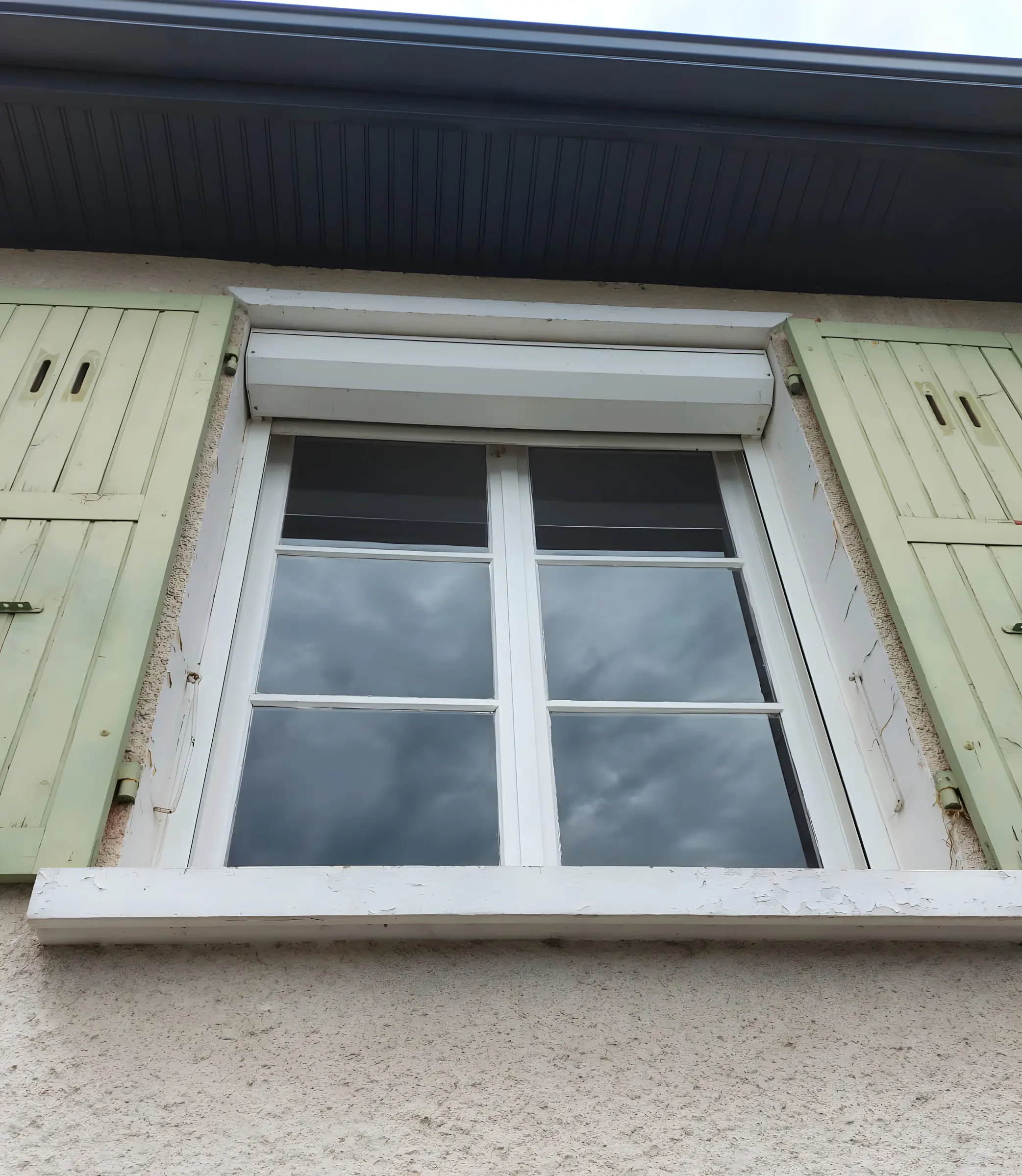 Ancienne fenêtre en bois blanc à petits carreaux vue d’en bas, coffre blanc au-dessus, volets battants vert pâle