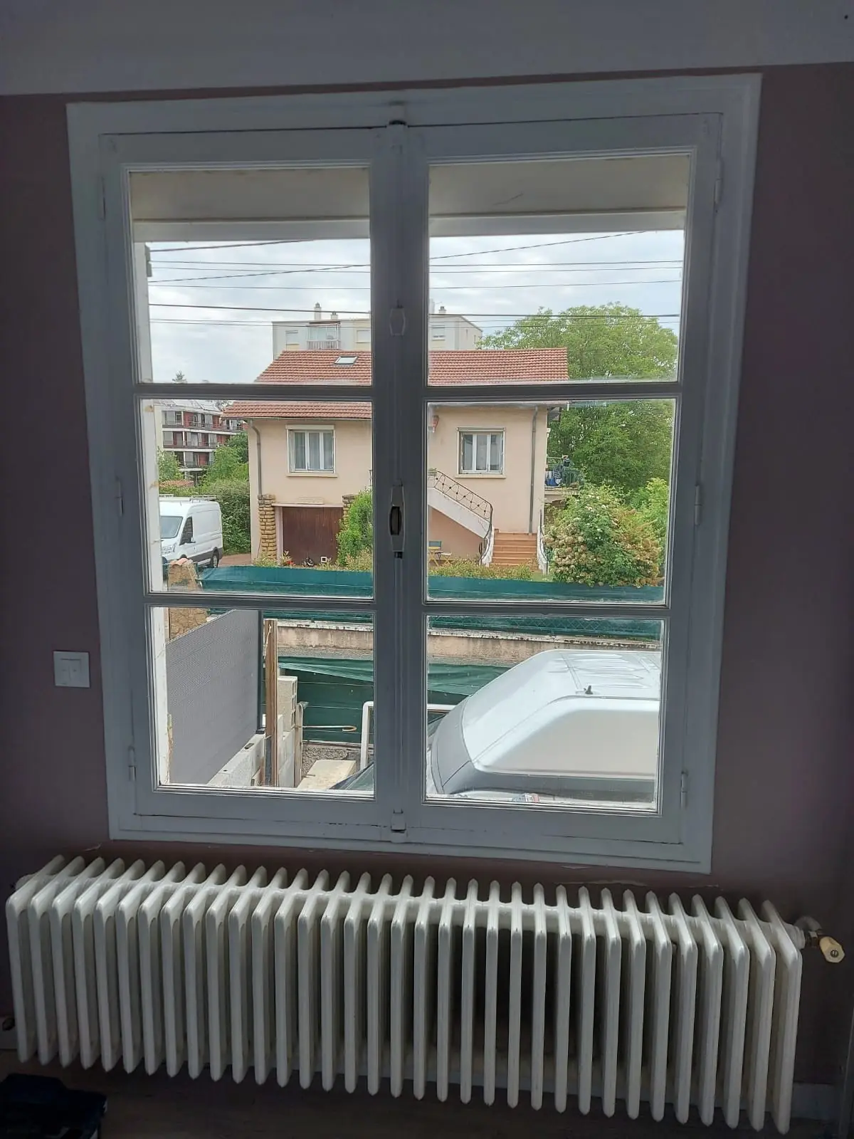 Ancienne fenêtre en bois blanc à petits carreaux vue de l’intérieur, radiateur en fonte dessous