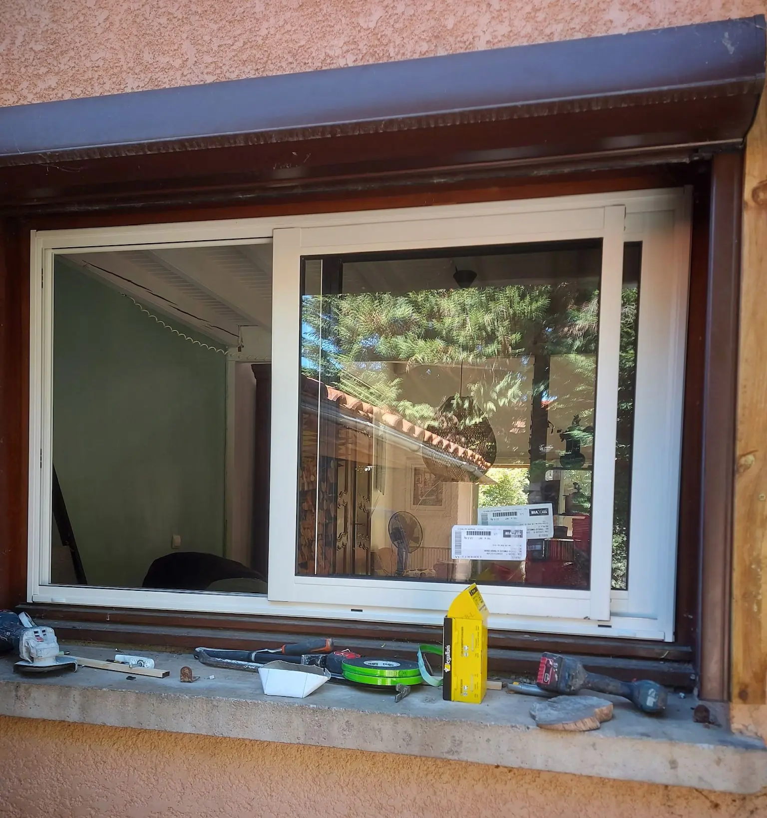 Fenêtre coulissante blanche neuve à deux vantaux dans un cadre brun, outils posés sur l’appui