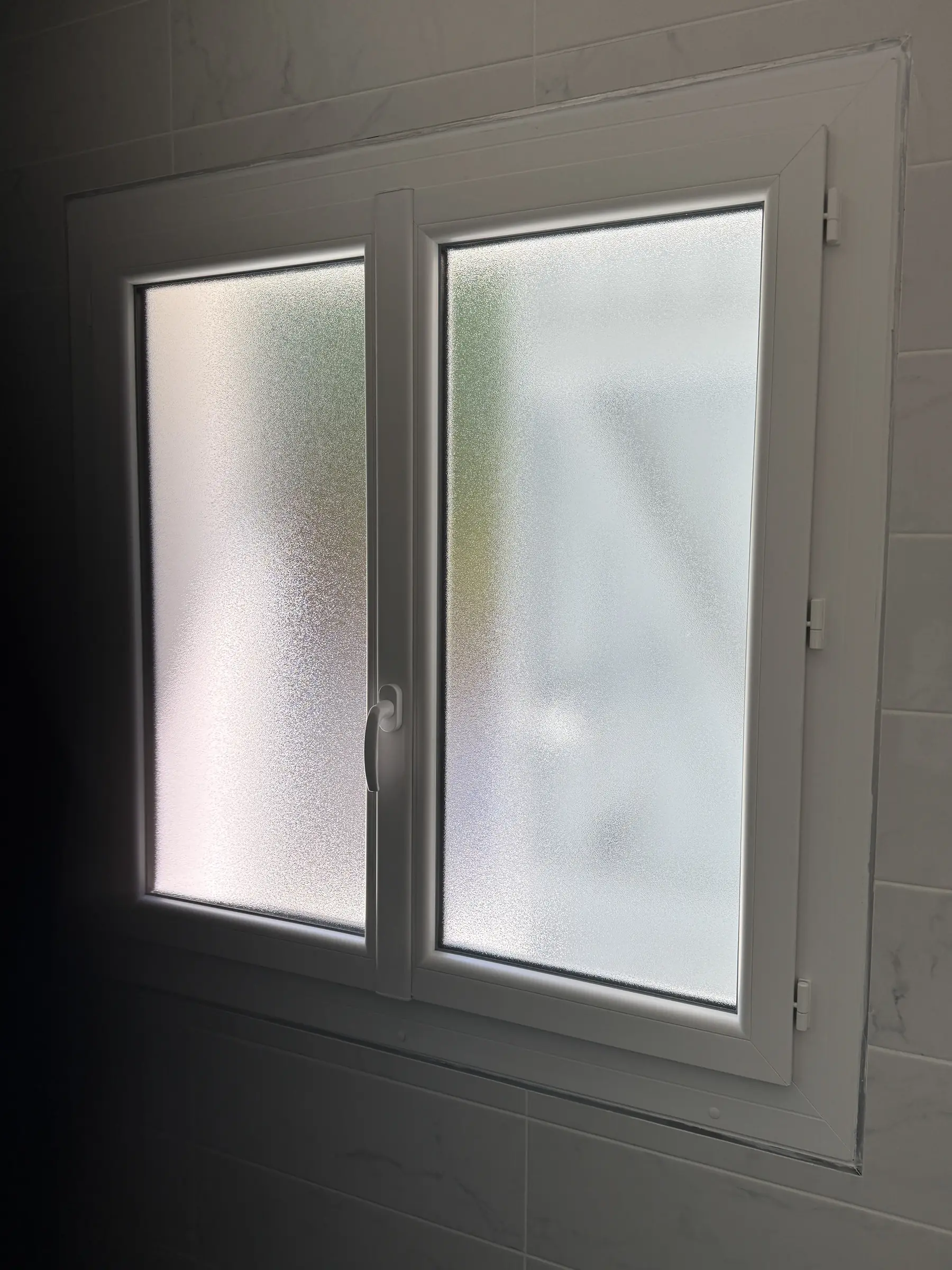 Fenêtre PVC blanche à deux vantaux en verre dépoli, habillage blanc, mur carrelé blanc