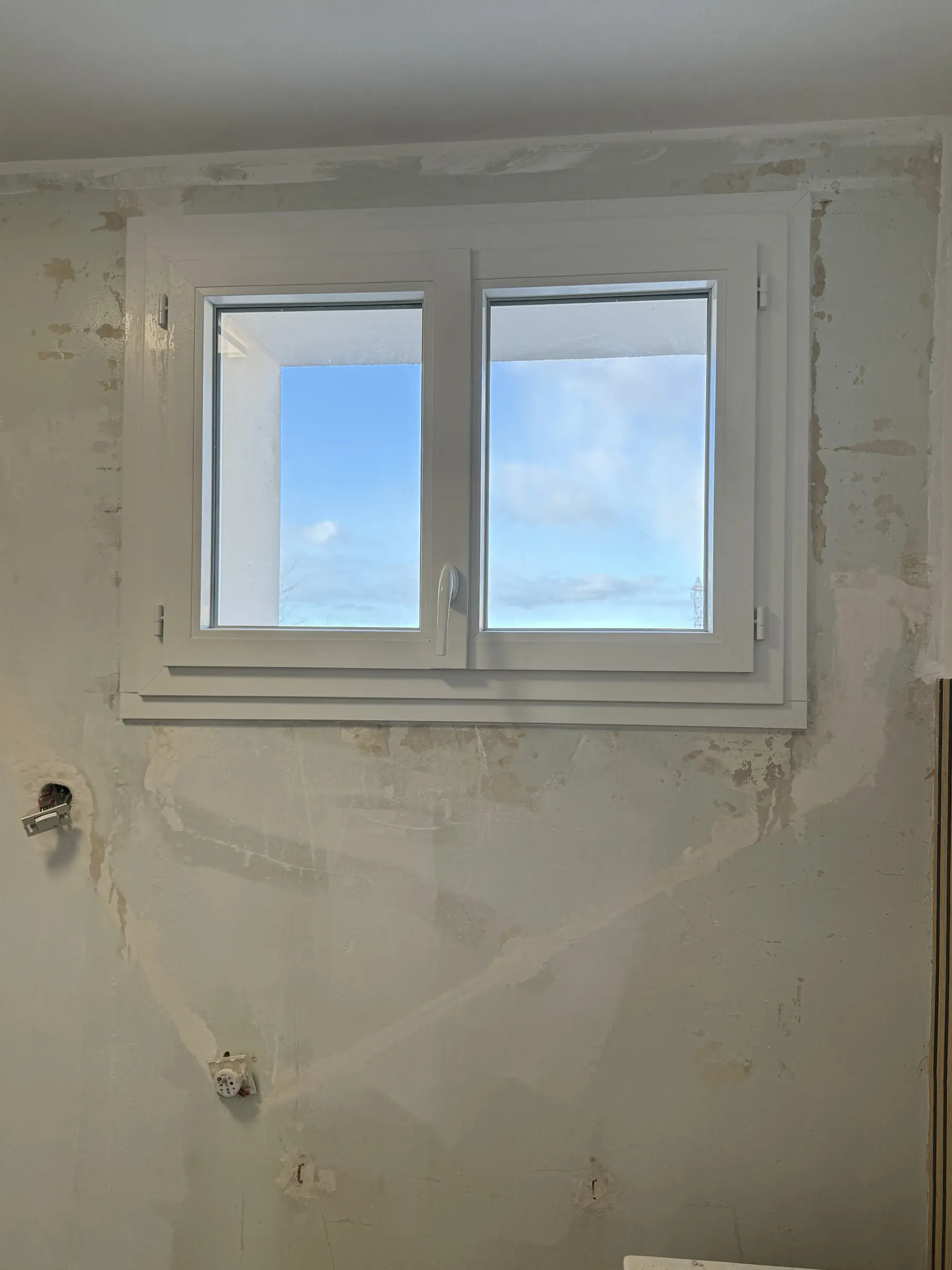Fenêtre PVC blanche neuve à deux vantaux vue de l’intérieur, habillage blanc autour du cadre