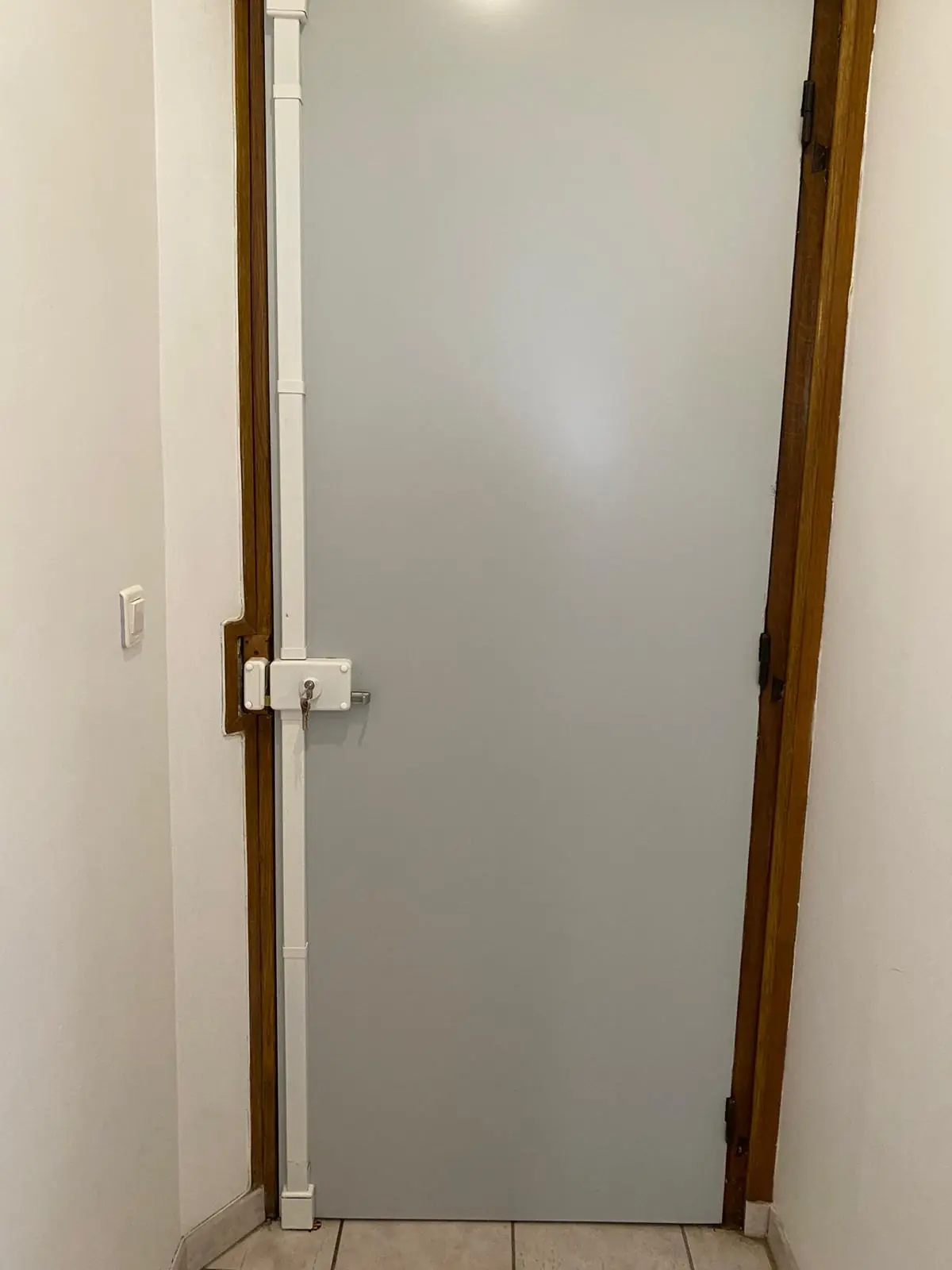 Porte d’appartement grise vue de l’intérieur, serrure en applique blanche et longue tringle verticale de verrouillage