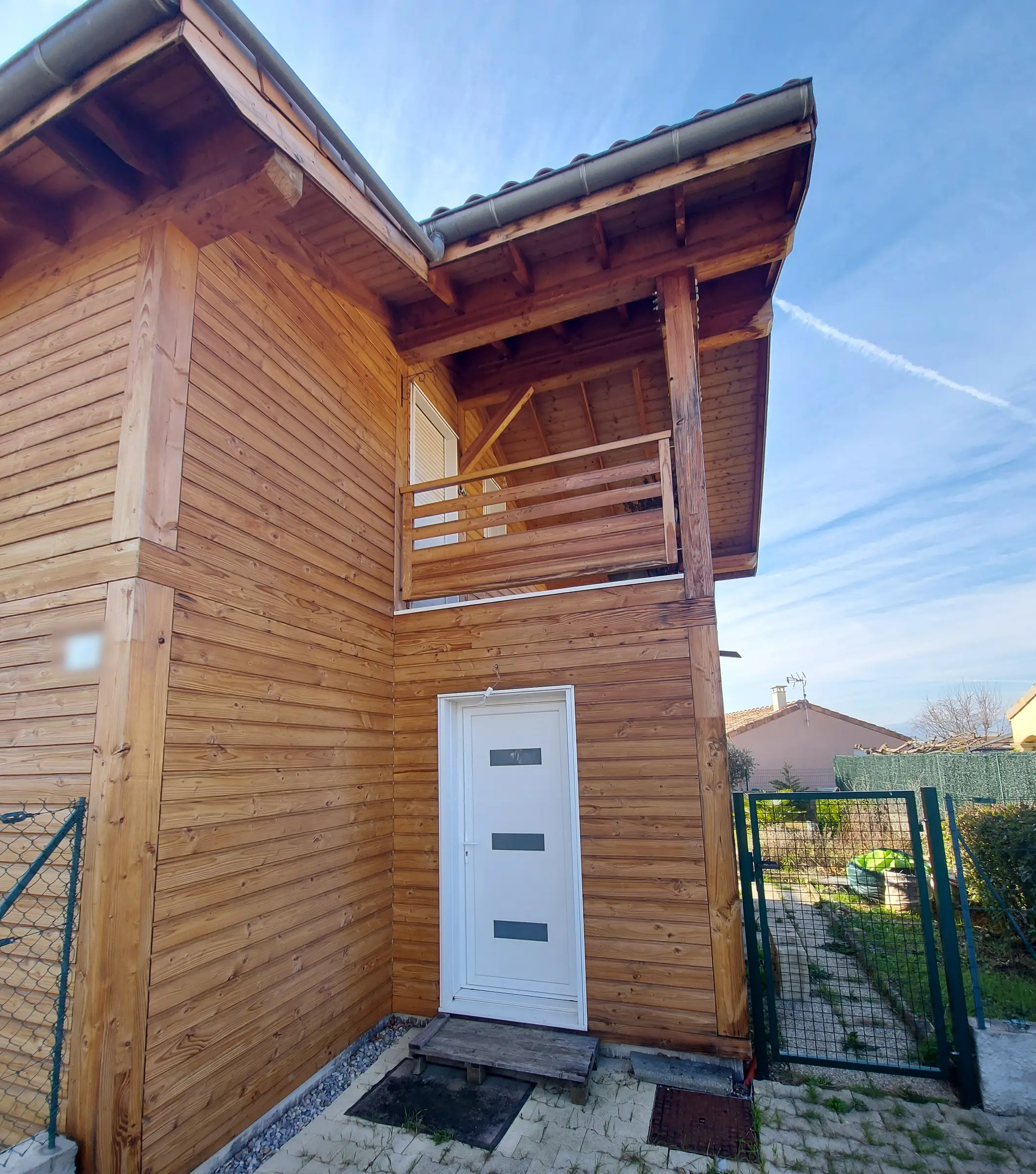Porte d’entrée PVC blanche à trois petits vitrages rectangulaires dans une façade en lames de bois