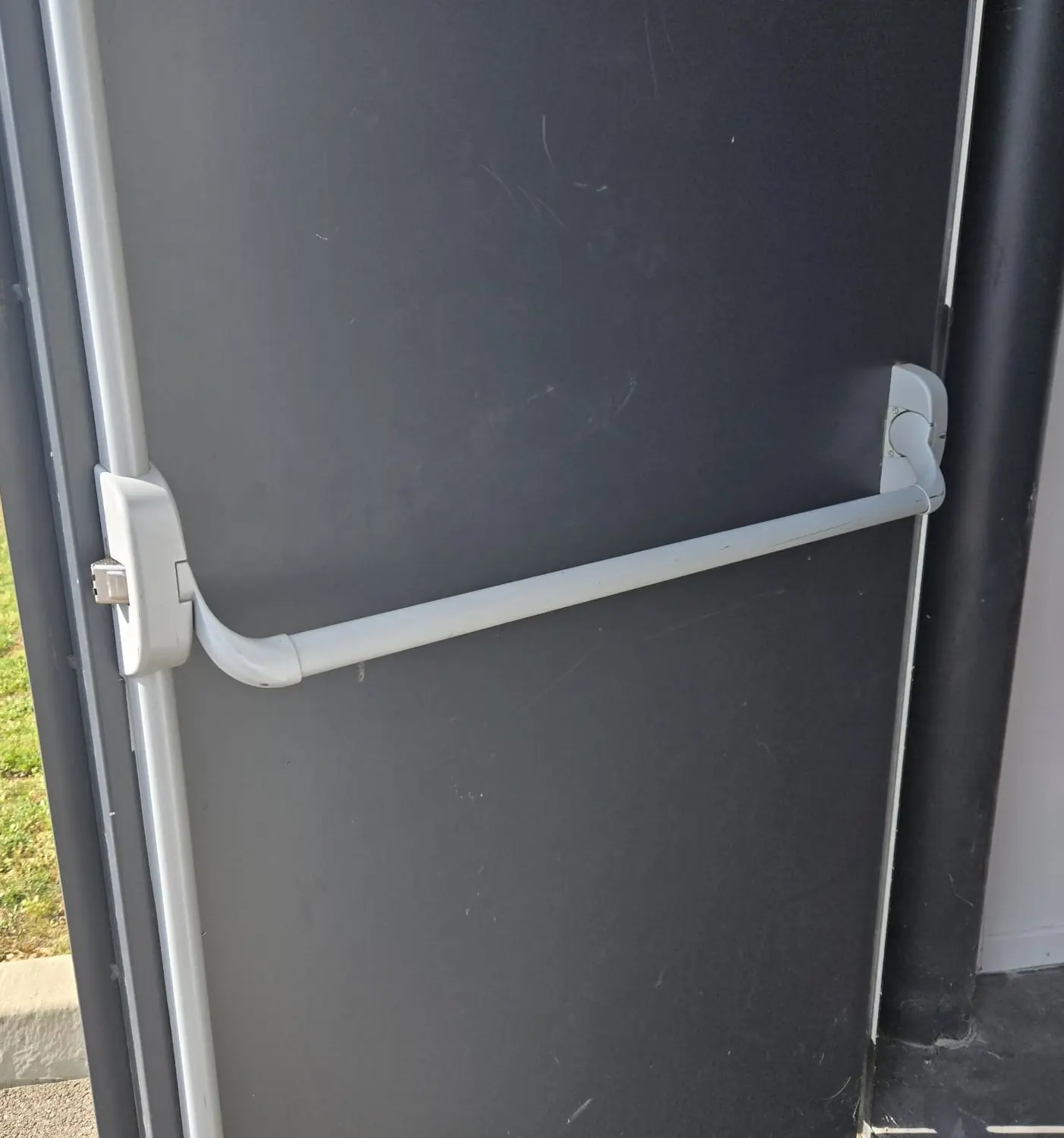 Face intérieure d’une porte métallique gris anthracite avec une barre anti-panique grise