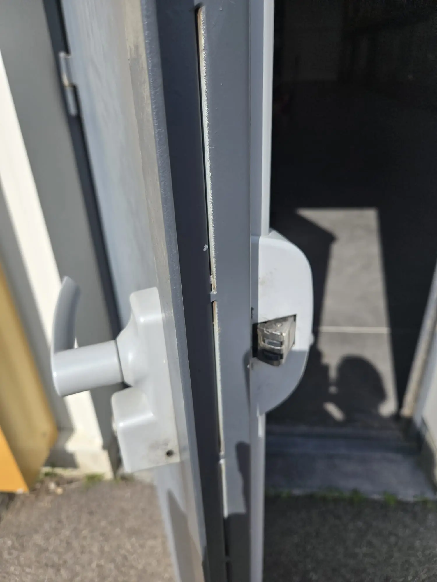 Porte métallique grise entrouverte, serrure en applique grise à béquille et gâche en applique avec son pêne