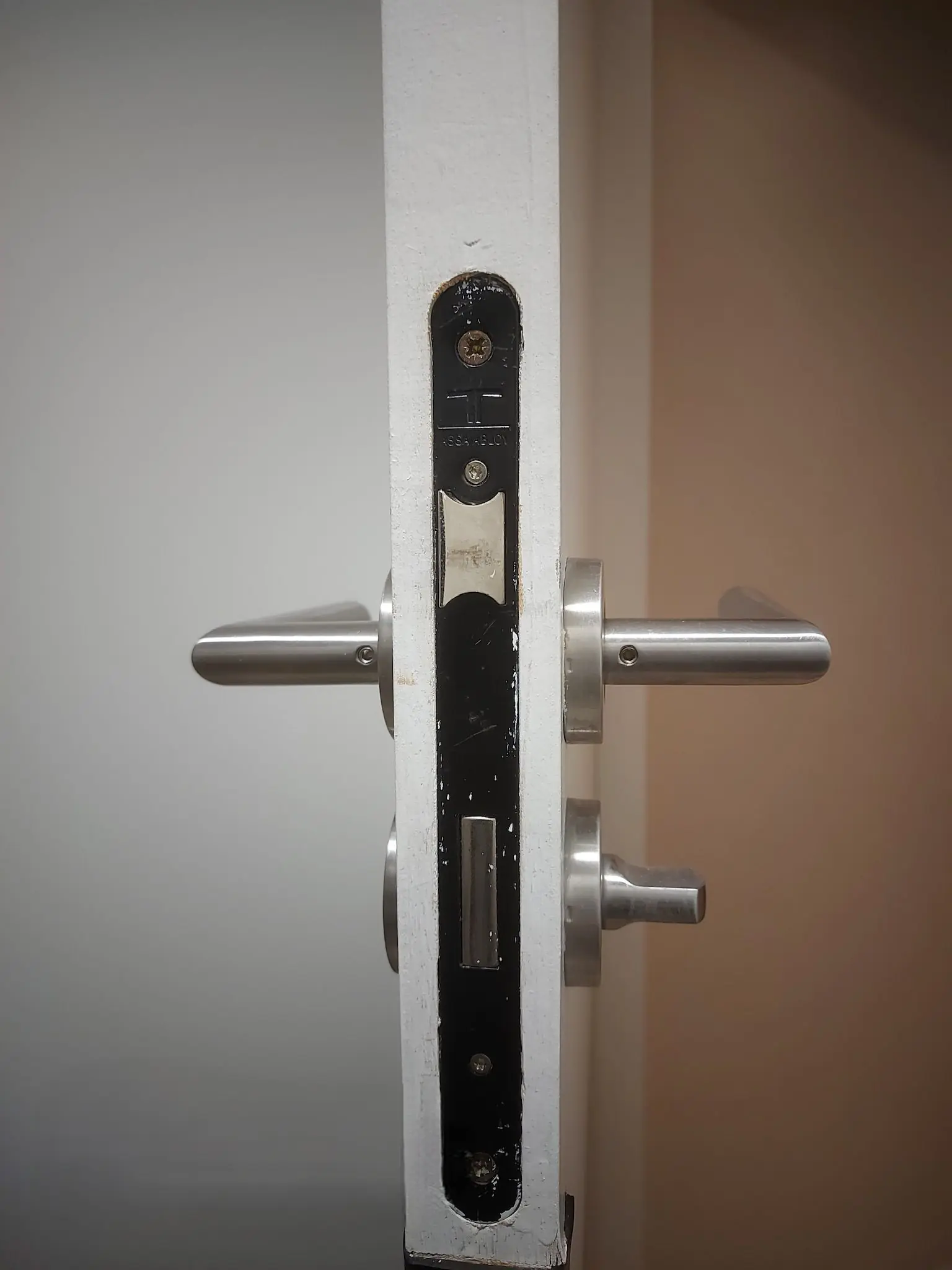 Chant d’une porte blanche avec une serrure encastrée neuve, béquilles inox et bouton de condamnation
